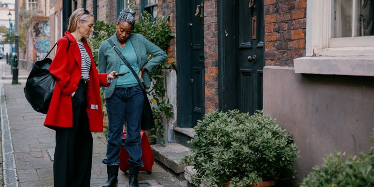Two women looking at tablet outside houses